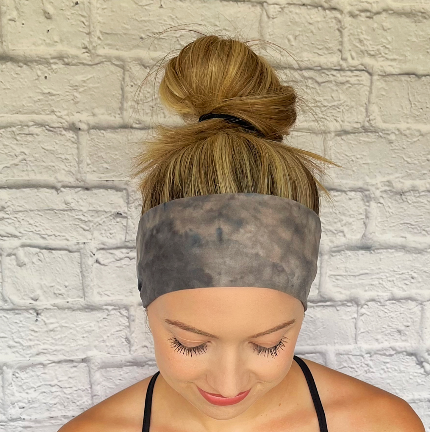 Woman with hair in bun wearing flat, stretchy, tie dye headband in gray and tan.