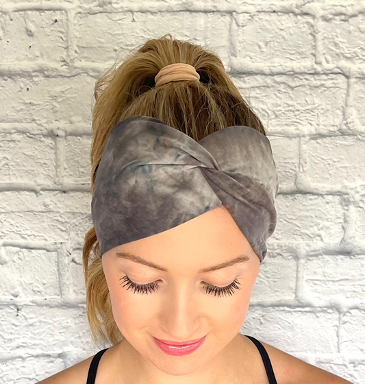 Woman with hair in curled ponytail wearing wide, twisted headband in gray tie dye print.