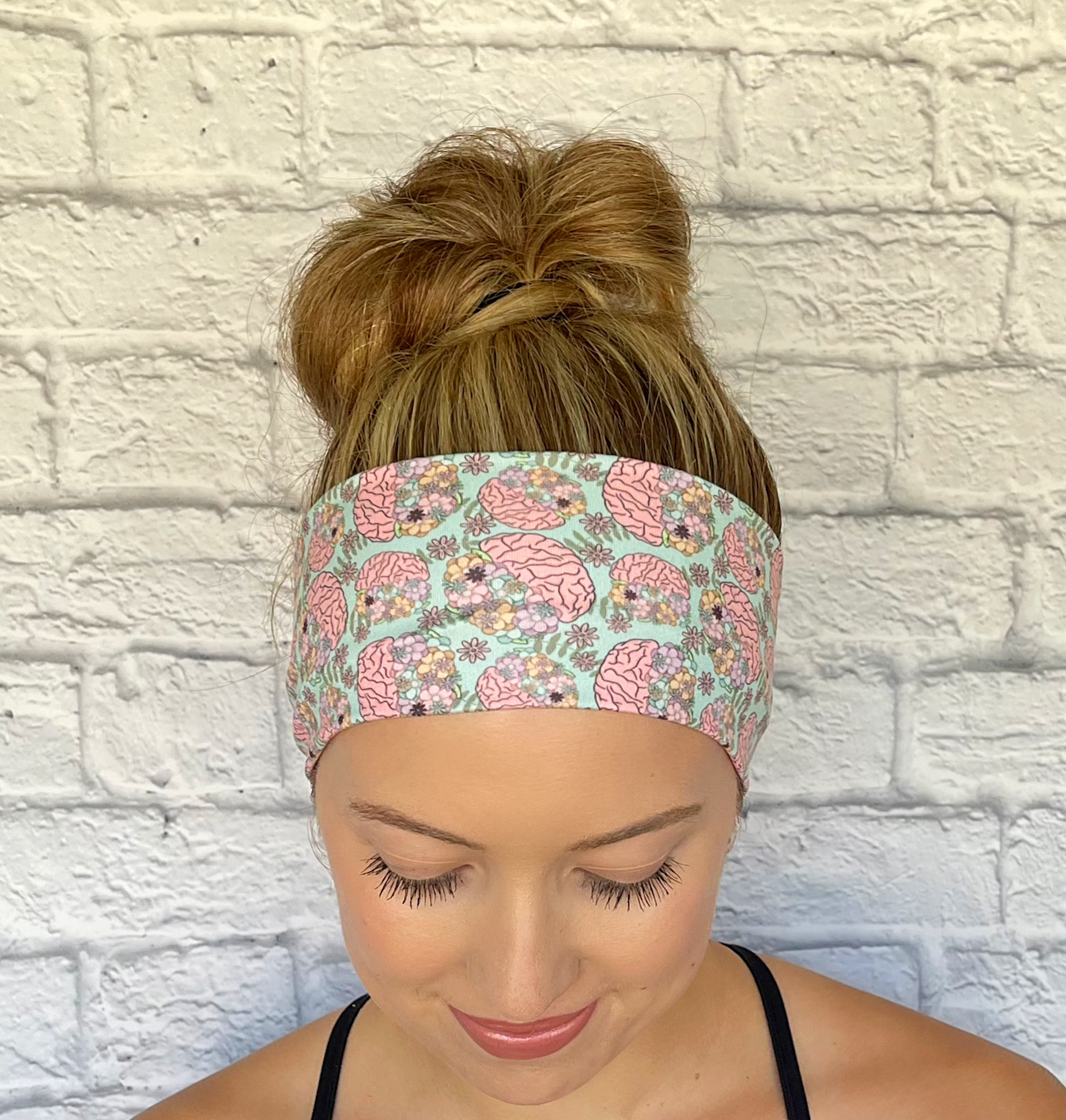 Woman with hair in bun wearing stretchy, mint green color headband with brain and floral print.