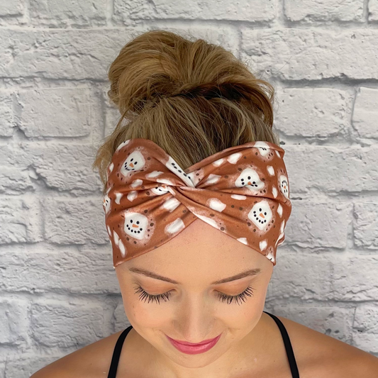 Woman with hair in bun wearing brown, wide, twisted headband with white snowman hot chocolate print.