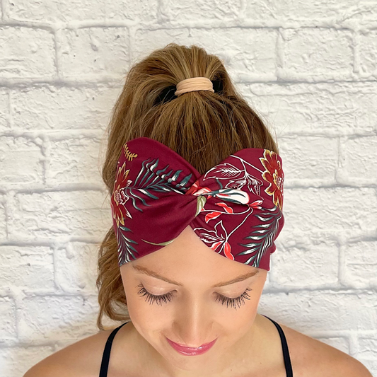 Woman with hair in ponytail wearing maroon color wide twist headband with Hawaiian theme flowers.