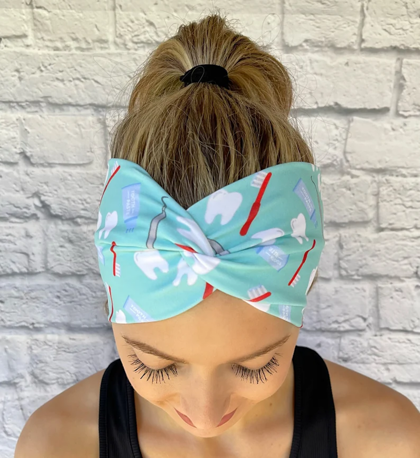 Woman with hair in curled ponytail wearing stretchy, wide, twisted headband in mint color with dental theme print.