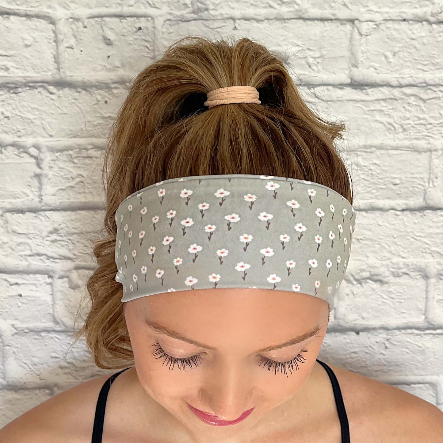 Woman wearing hair in ponytail with mint color headband with small white flowers.