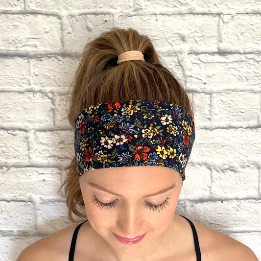 Woman with hair in ponytail wearing headband in navy color with small flower print in yellow, red, blue, and white.