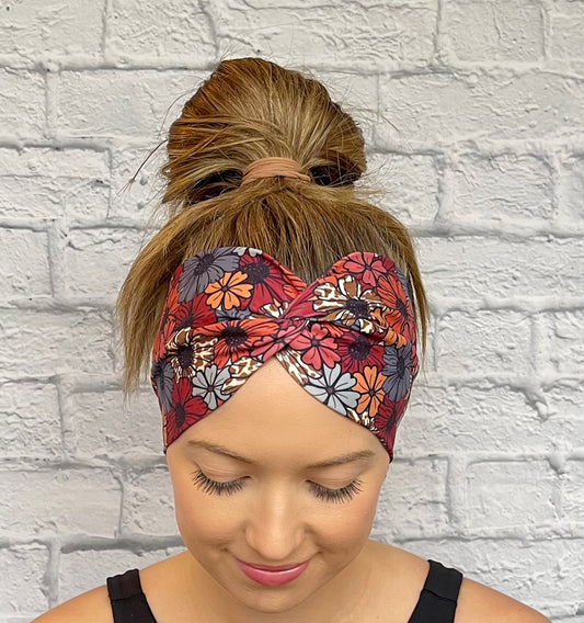 Woman with hair in bun wearing wide, twisted headband in floral print with a navy/red color base with other colors within.