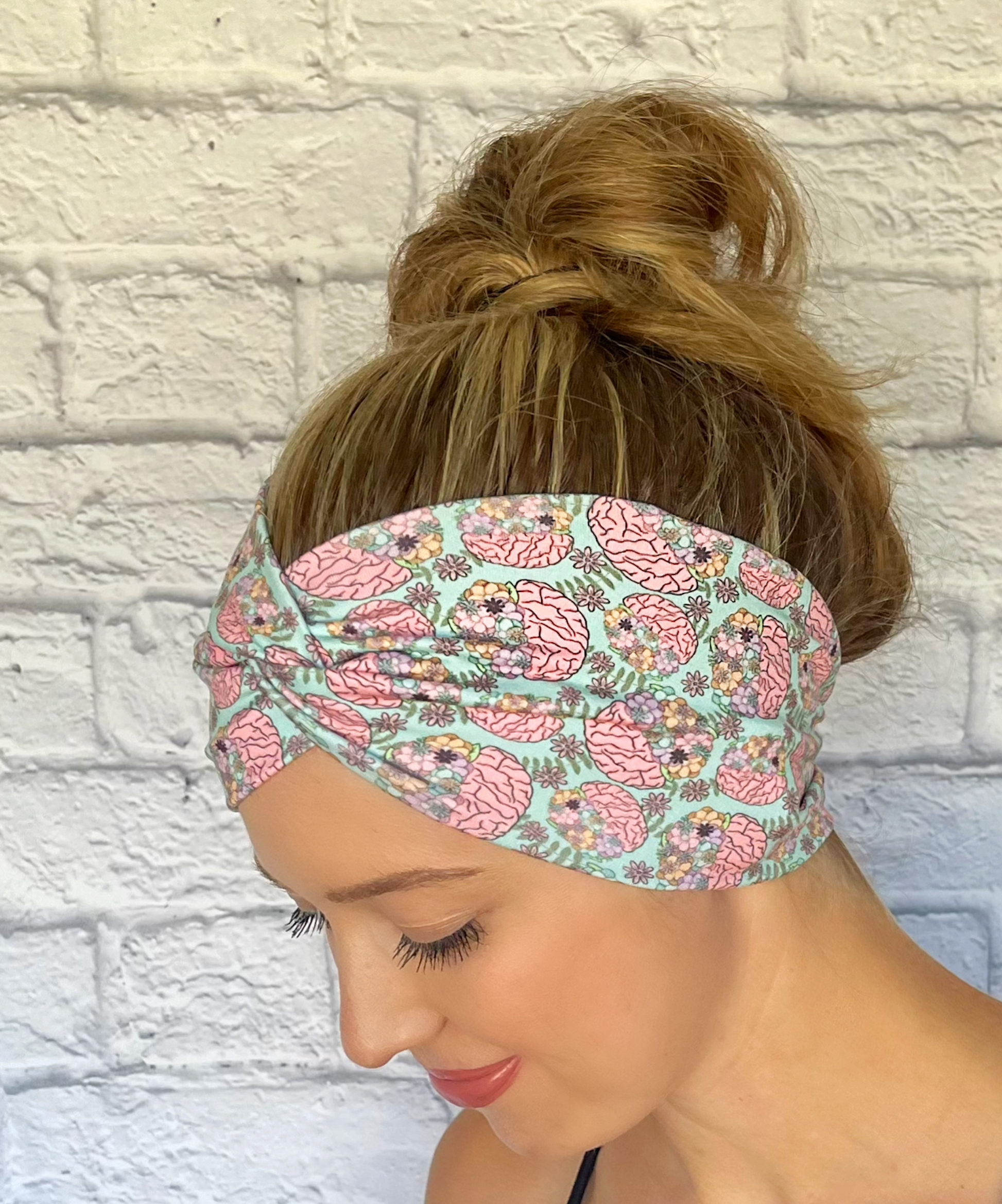 Woman with hair in bun wearing wide, twisted headband in mint green color with brain and flower print.