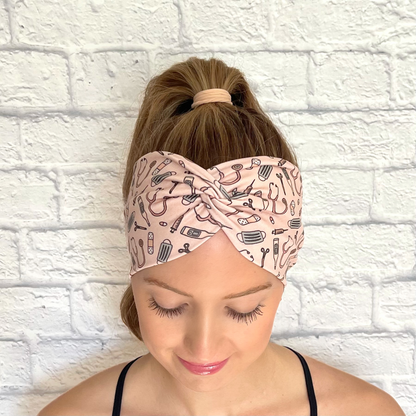 Woman with hair in curled ponytail wearing wide, twisted headband in peach color with medical theme print.