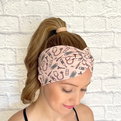 Woman with hair in curled ponytail wearing wide, twisted headband in peach color with medical theme print.