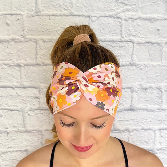 Woman with hair in curled ponytail wearing wide, twisted headband in peach color with light and dark pink, navy, white, yellow, and orange flower print.