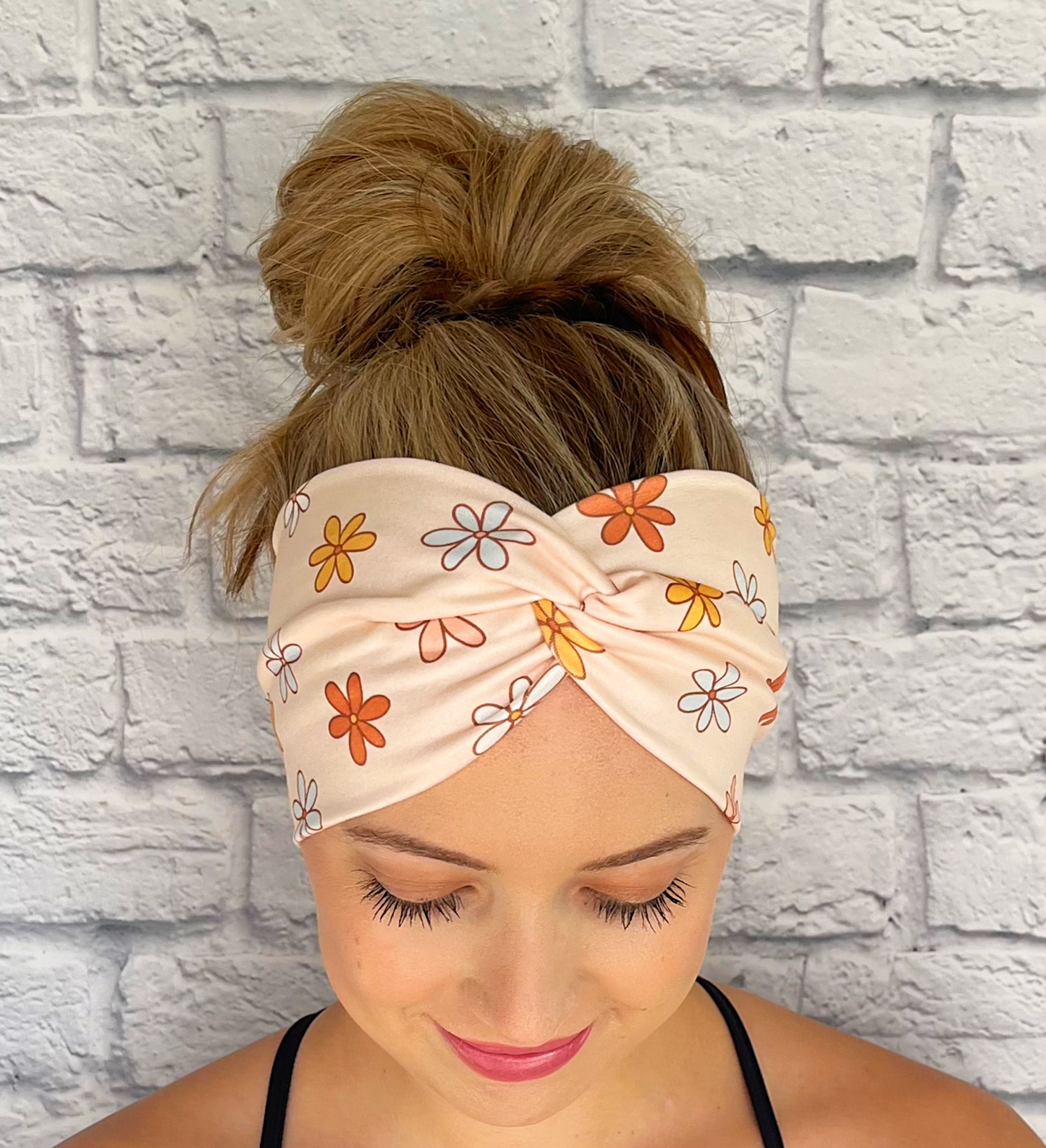 Woman with hair in bun wearing peach/cream color wide twisted headband with floral print.