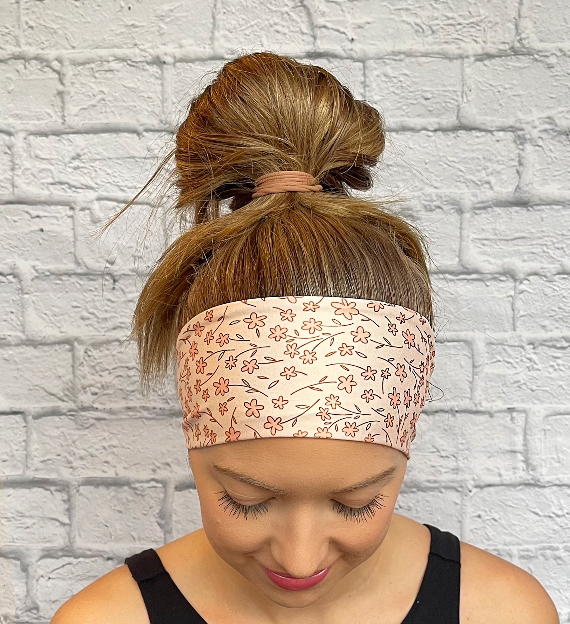 Woman with hair in bun wearing flat, stretchy, peach color headband with small peach/tan flower print.