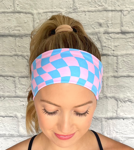 Woman wearing a pink and blue checkered headband against a white brick wall.