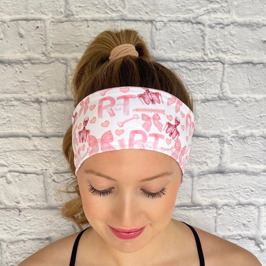 Woman with hair in curled ponytail wearing stretchy, white headband with pink "RT" and "radiology tech" print, pink skeletons, pink bow, and pink hearts.