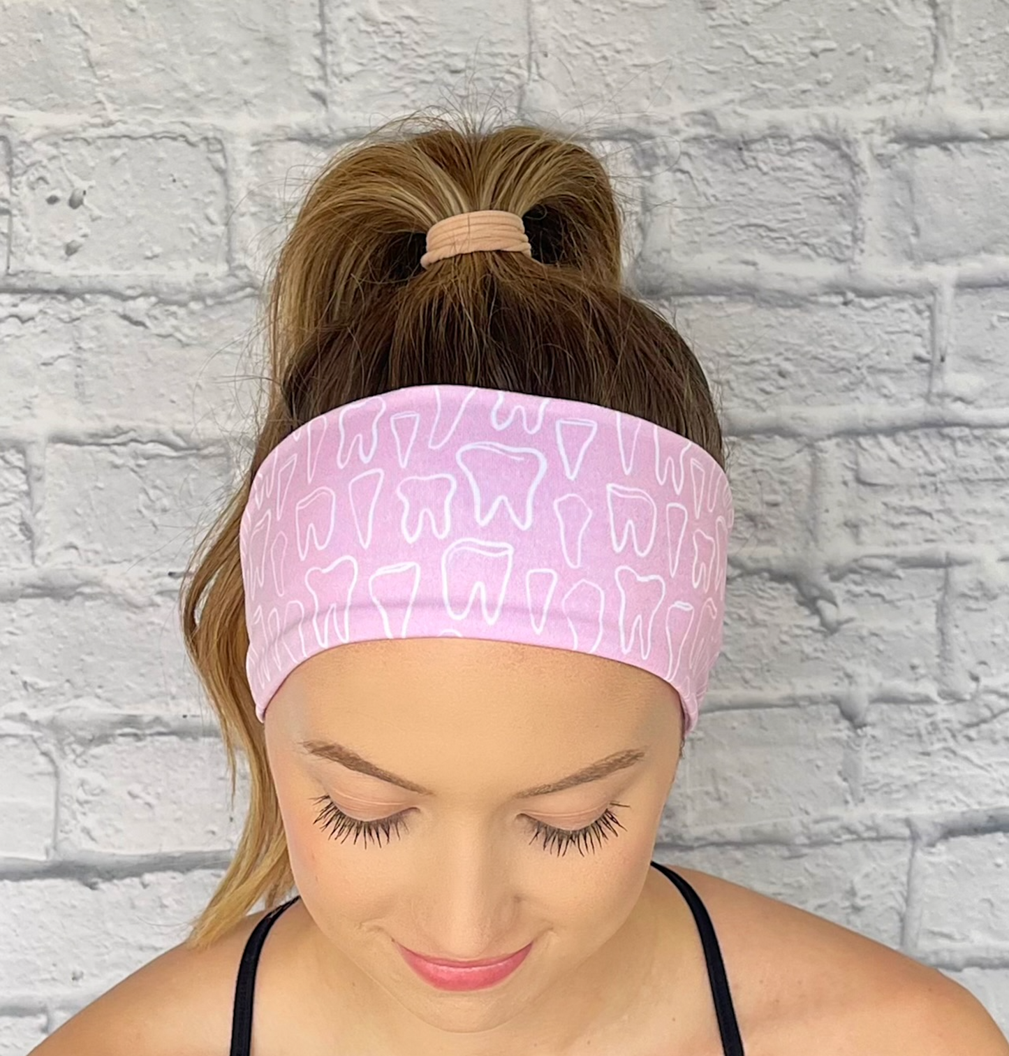 Woman with hair in curled ponytail wearing stretchy, light pink headband with white teeth print.