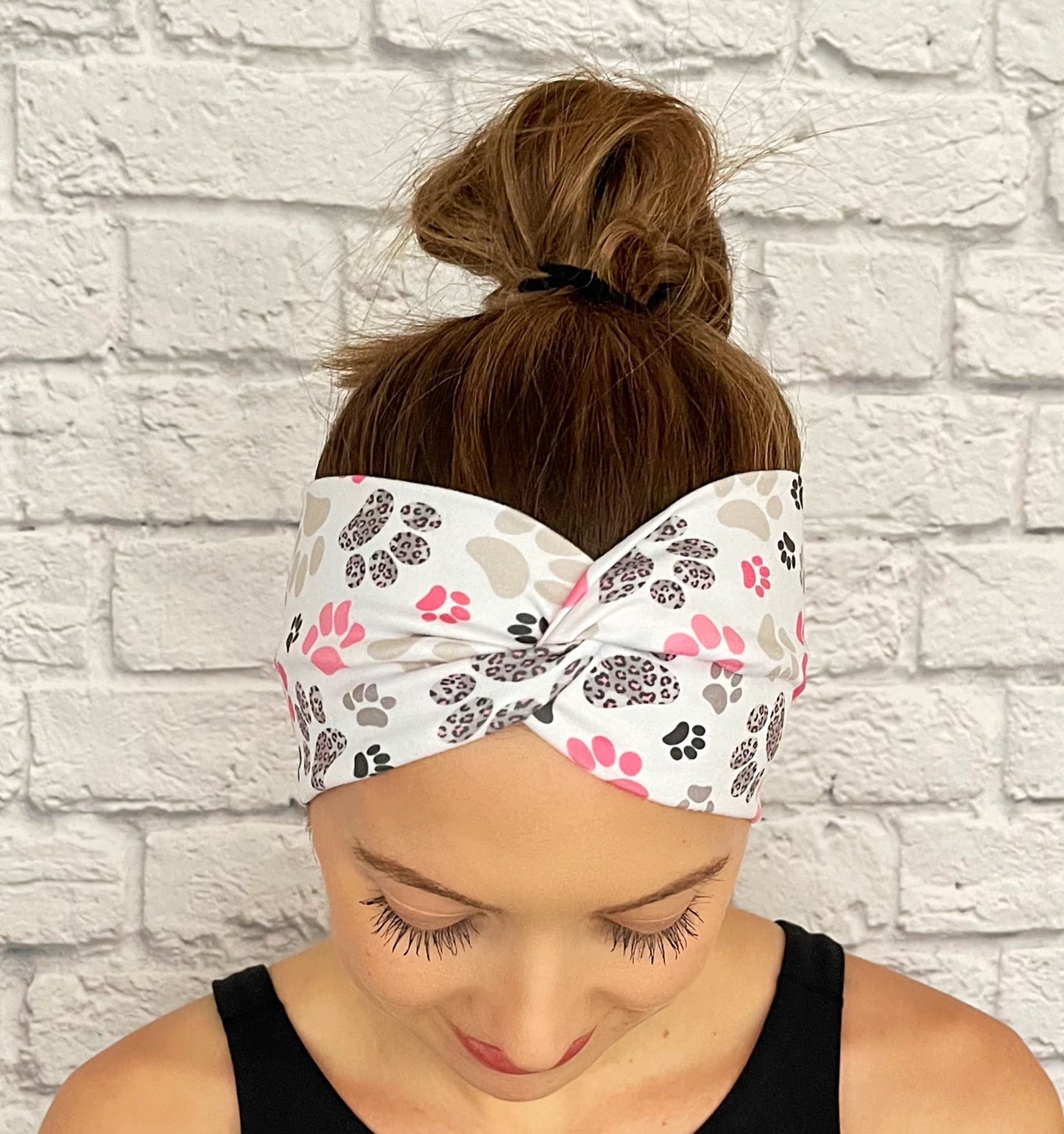 Woman with hair in bun wearing wide, twisted headband in white with pink, gray, and black paw print.