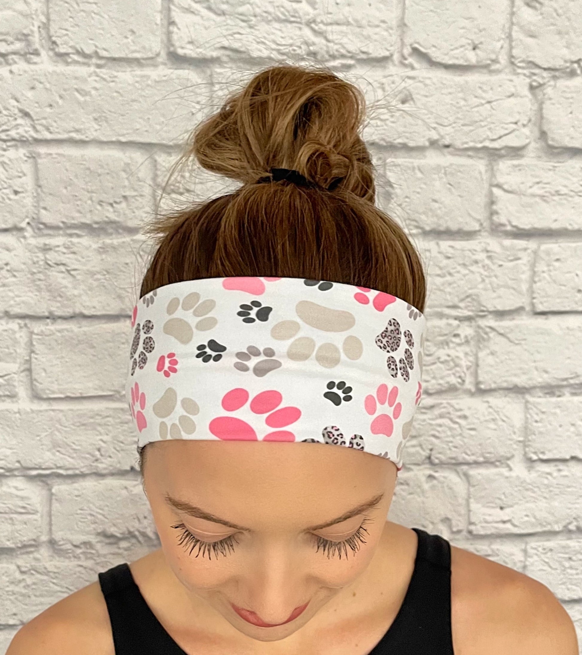 Woman with hair in bun wearing flat, stretchy headband in white with pink, gray, and black paw print.