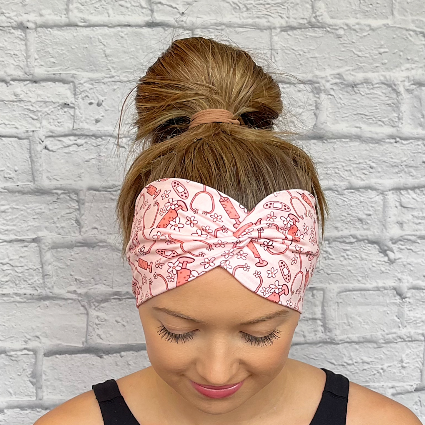 Woman wearing wide, twisted headband in pink with flowers, stethoscopes, bandages, and syringes.