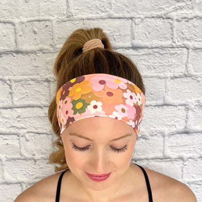 Woman with hair in curled ponytail wearing flat headband in peach color with light and dark pink, navy, white, yellow, and orange flower print.