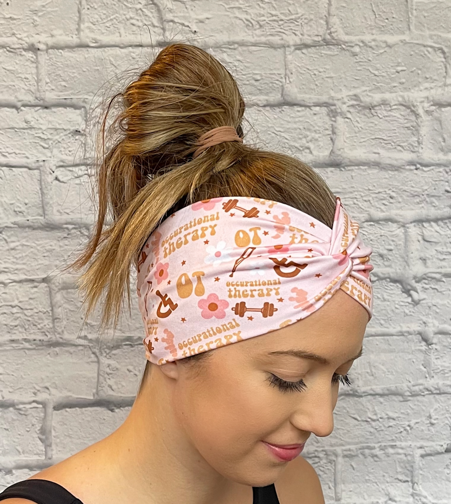 Woman with hair in bun wearing wide, twisted, pink headband with print- OT, occupational therapy with flowers, crutches, a wheelchair, and weights. 