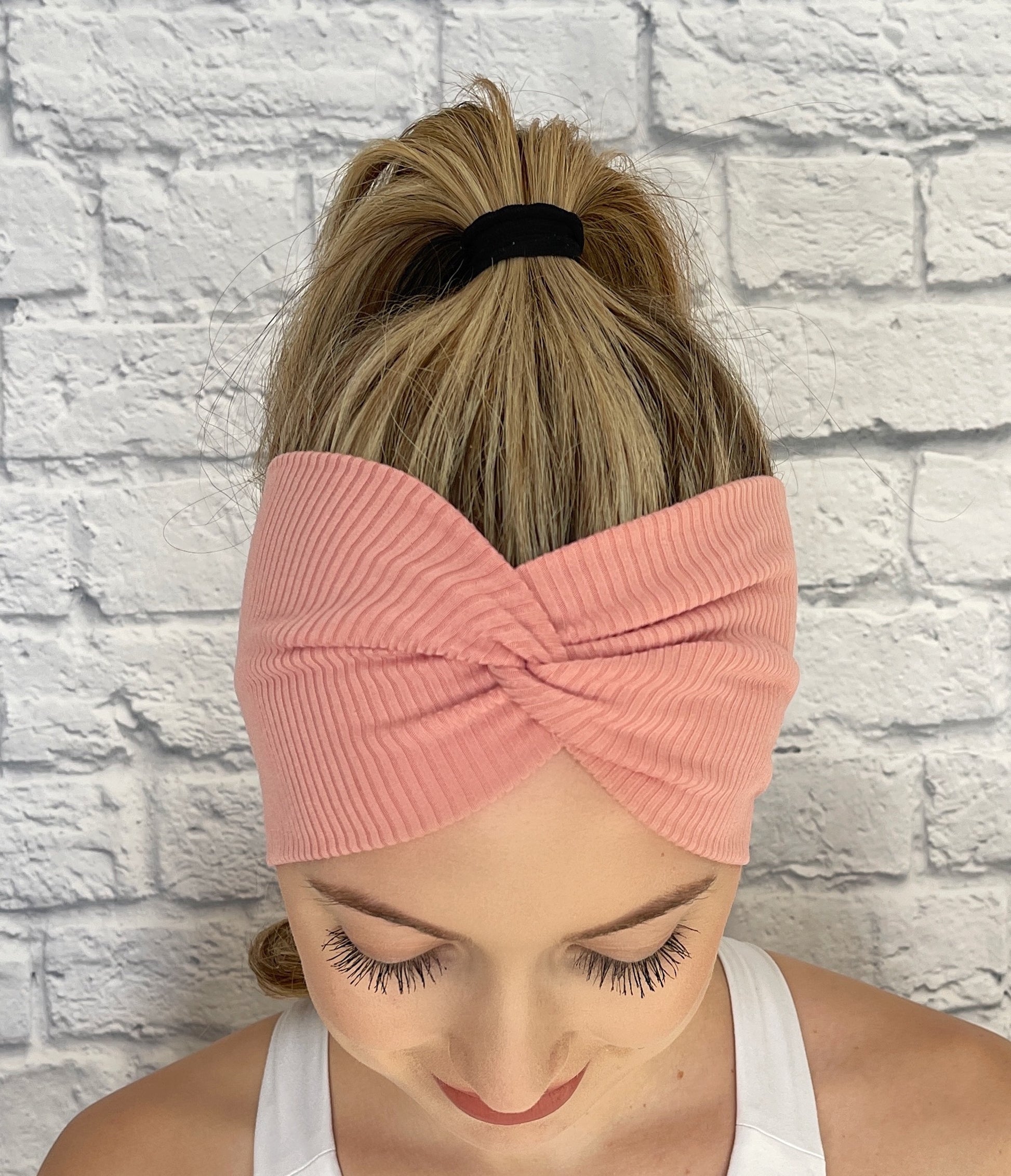 Woman with hair in ponytail wearing wide, twisted headband with pink ribbed fabric.