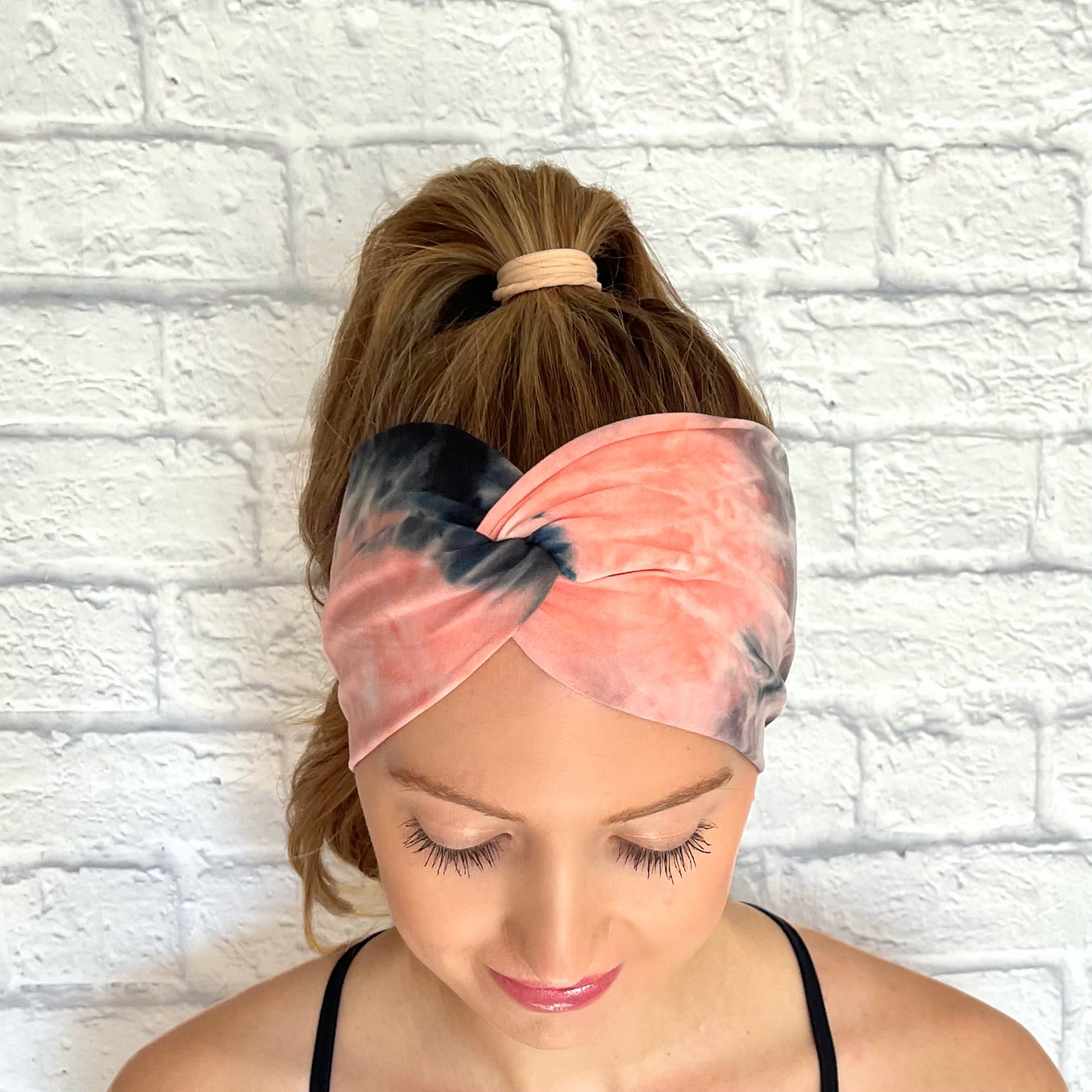 Woman with hair in curled ponytail wearing wide, twisted, pink, white, and gray/black tie dye headband.