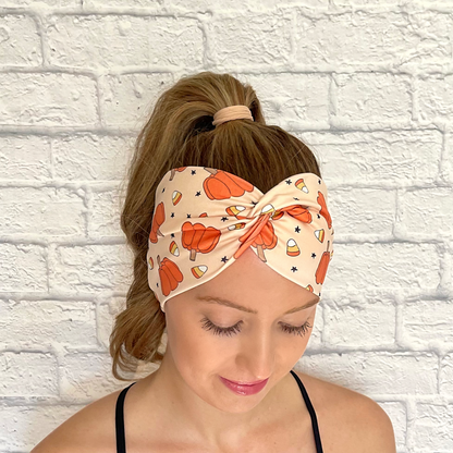 Woman with hair in curled ponytail wearing wide, twisted headband in tan with pumpkin, candy corn, and star print.