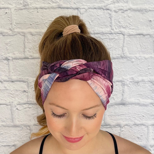 Woman with hair in curled ponytail wearing pink and purple tie dye, ribbed, knotted headband in ribbed fabric.