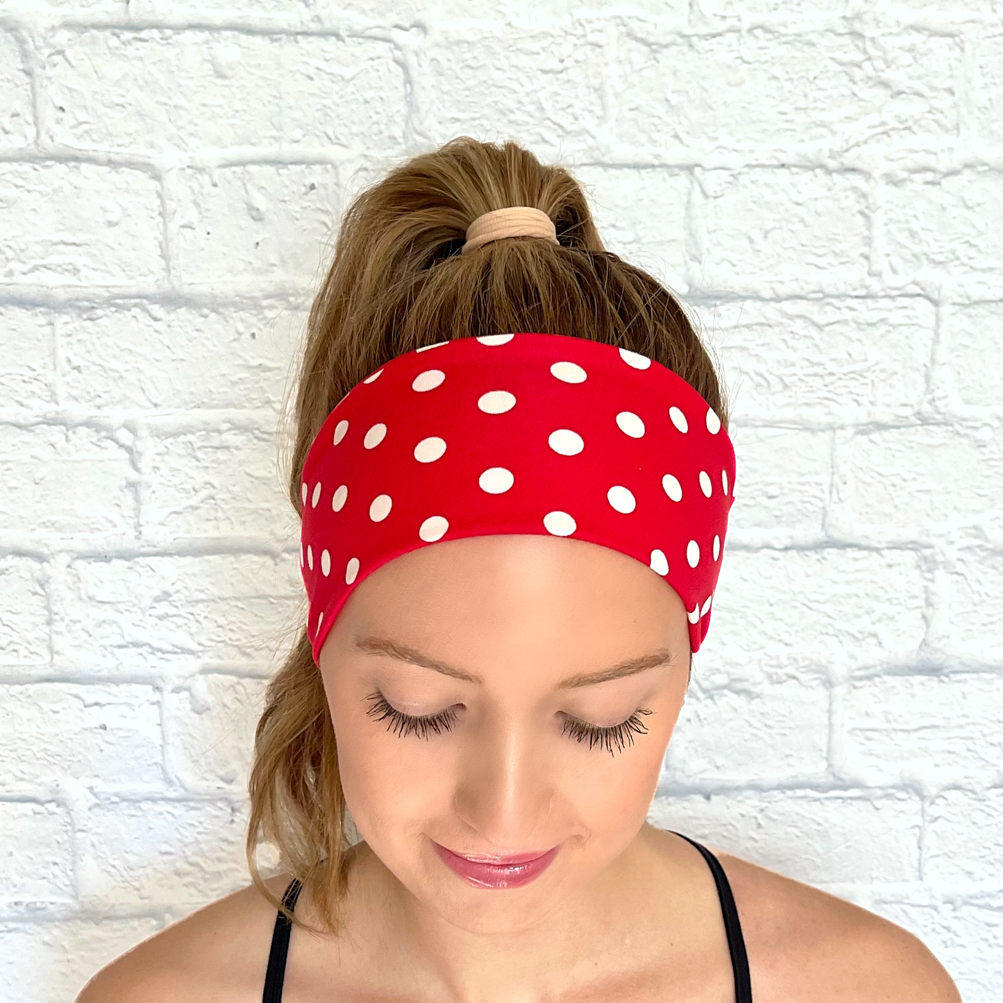 Woman with hair in ponytail wearing red headband with white polka dots.