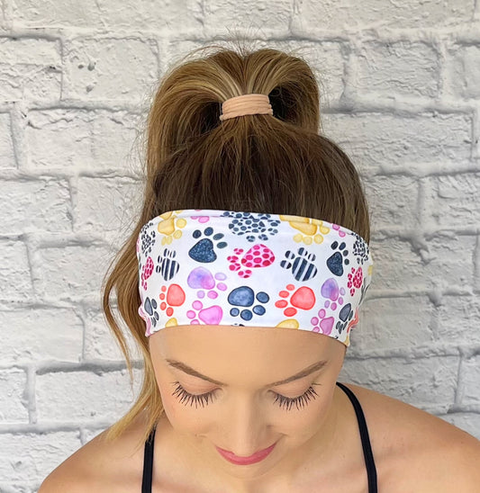 Woman with hair in curled ponytail wearing flat, stretchy, white headband with multi-color dog paw print.