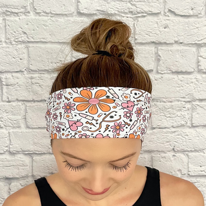 Woman wearing white headband with orange and pink medical theme print. Contains hearts, flowers, stethoscopes, bandages, and syringes.