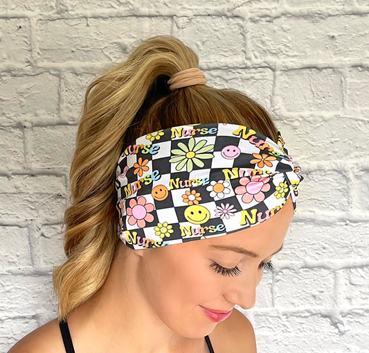 Woman with hair in curled ponytail wearing black and white checker print wide twist headband with "nurse" print and flowers in rainbow colors.