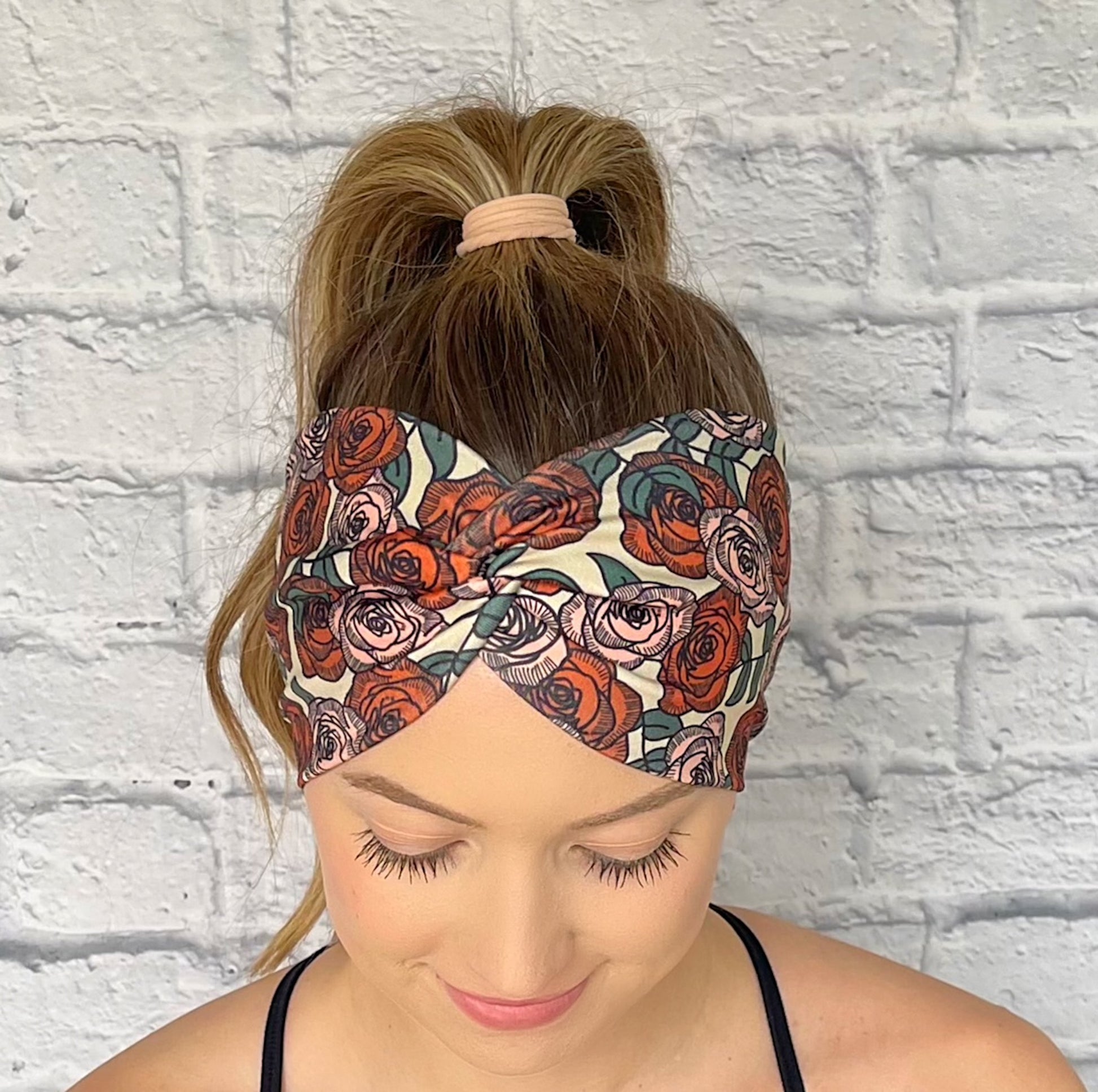 Woman with hair in curled ponytail wearing wide, twisted headband in cream with red and pink rose print.