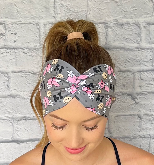 Woman with hair in curled ponytail wearing wide, twisted headband in gray with "RT" print, lungs, flowers, and smiley faces.