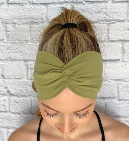 Woman with hair in ponytail wearing wide, twisted, sage green color headband.