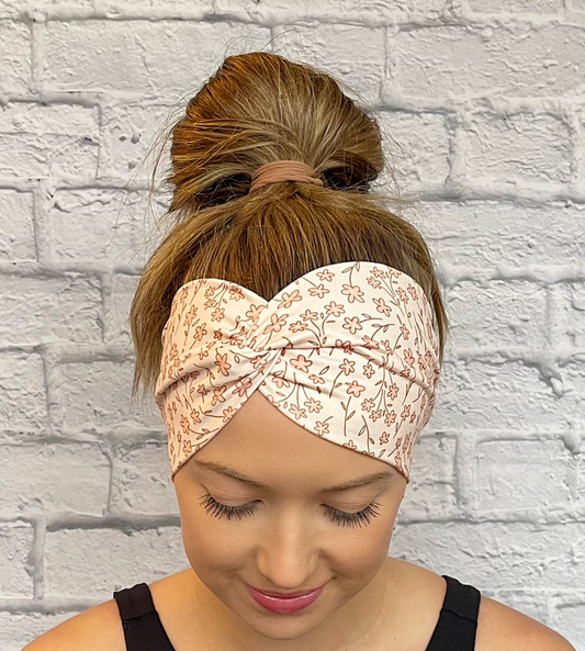 Woman with hair in bun wearing wide, twisted headband in peach/cream color with peach/cream/tan small flower print.