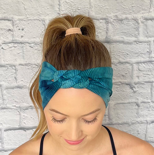 Woman with hair in curled ponytail wearing sailot knot style headband in ribbed, teal tie dye fabric.