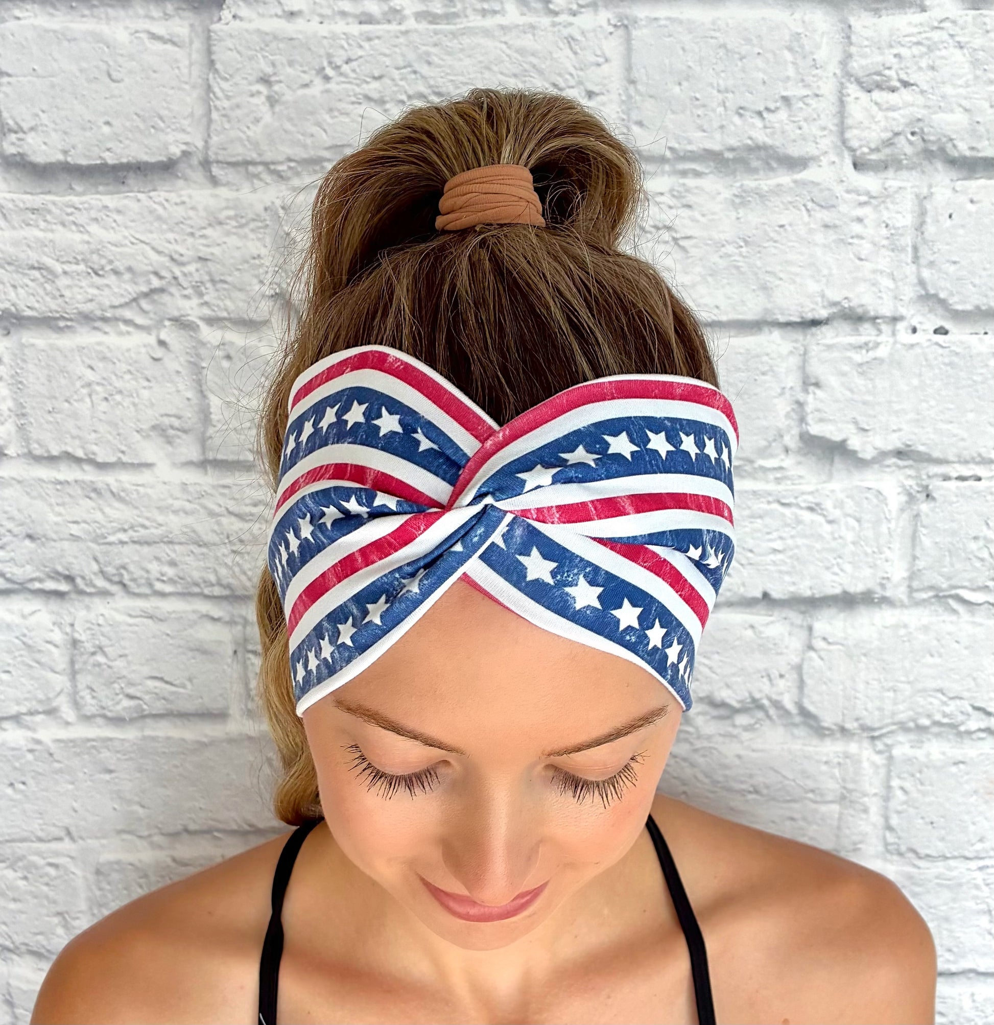 Woman with hair in ponytail wearing white wide twist headband with American Flag theme print.