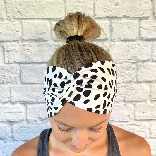 Woman with hair in bun wearing wide, twisted headband in white with black damatian print.