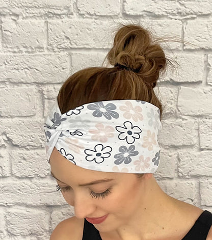 Woman with hair in bun wearing wide, twisted, white headband with floral print in light pink, gray, and black.