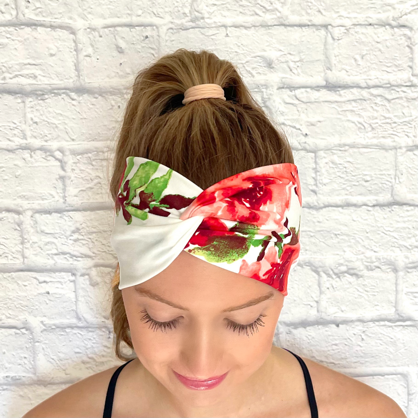 Woman with hair in ponytail wearing wide, twisted headband in white color with red floral rose print.