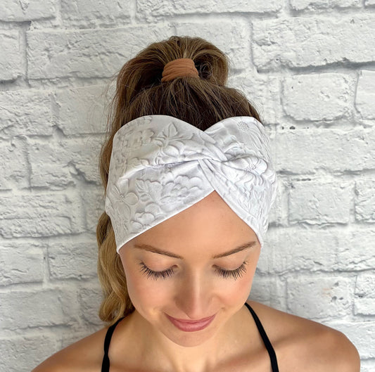 Woman with hair in ponytail wearing wide, twisted, white headband with faux embossed floral print and gray shadowing.