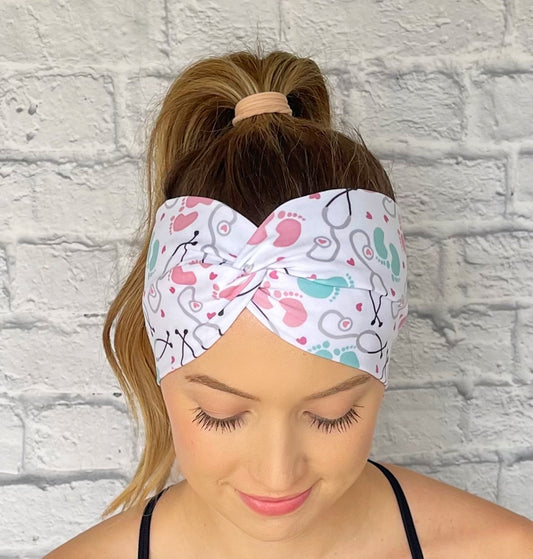 Woman wearing a white, OBGYN baby themed headband against a white brick wall.