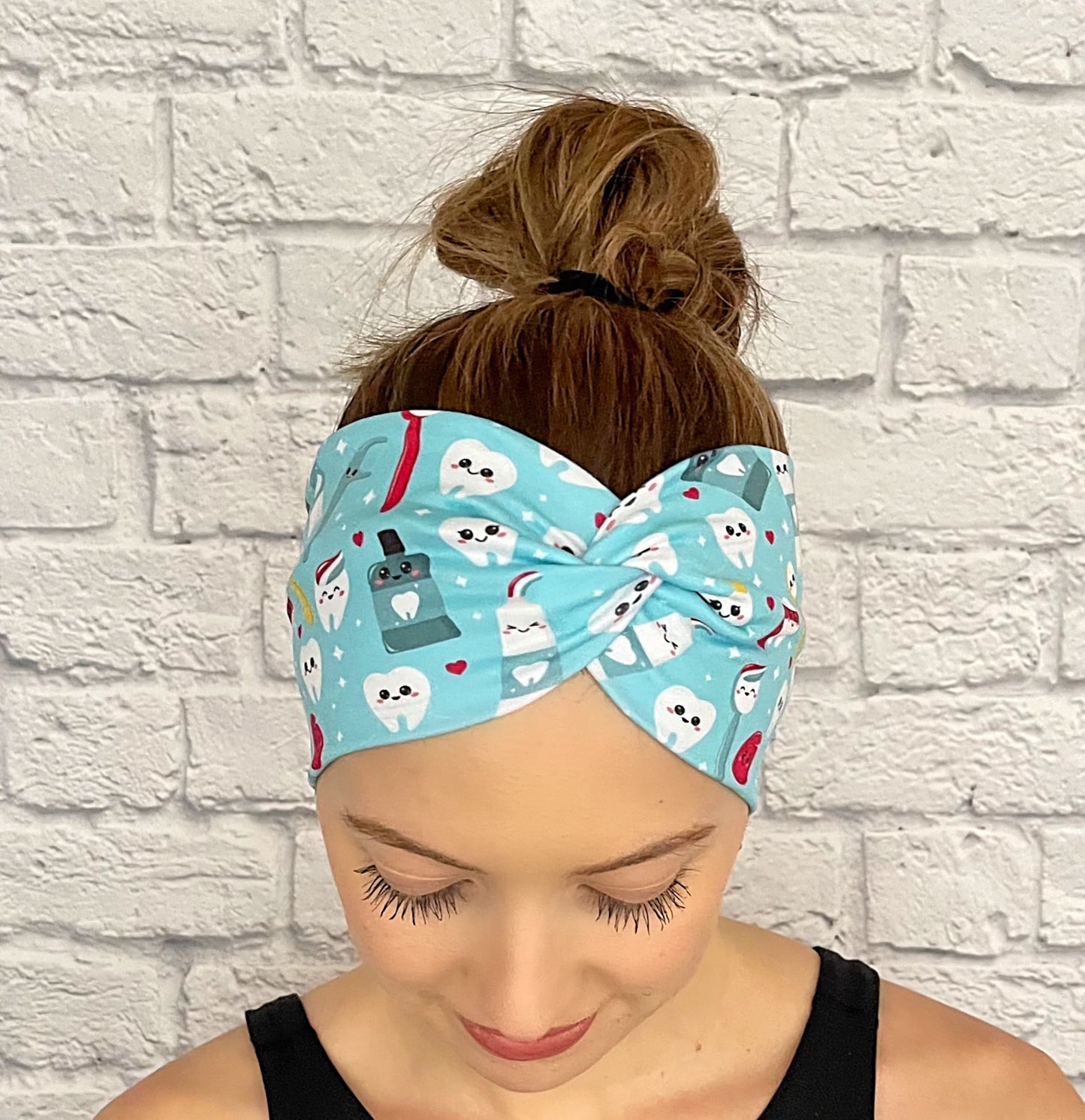 Woman with hair in bun wearing wide, twisted headband in light blue with dental theme print.