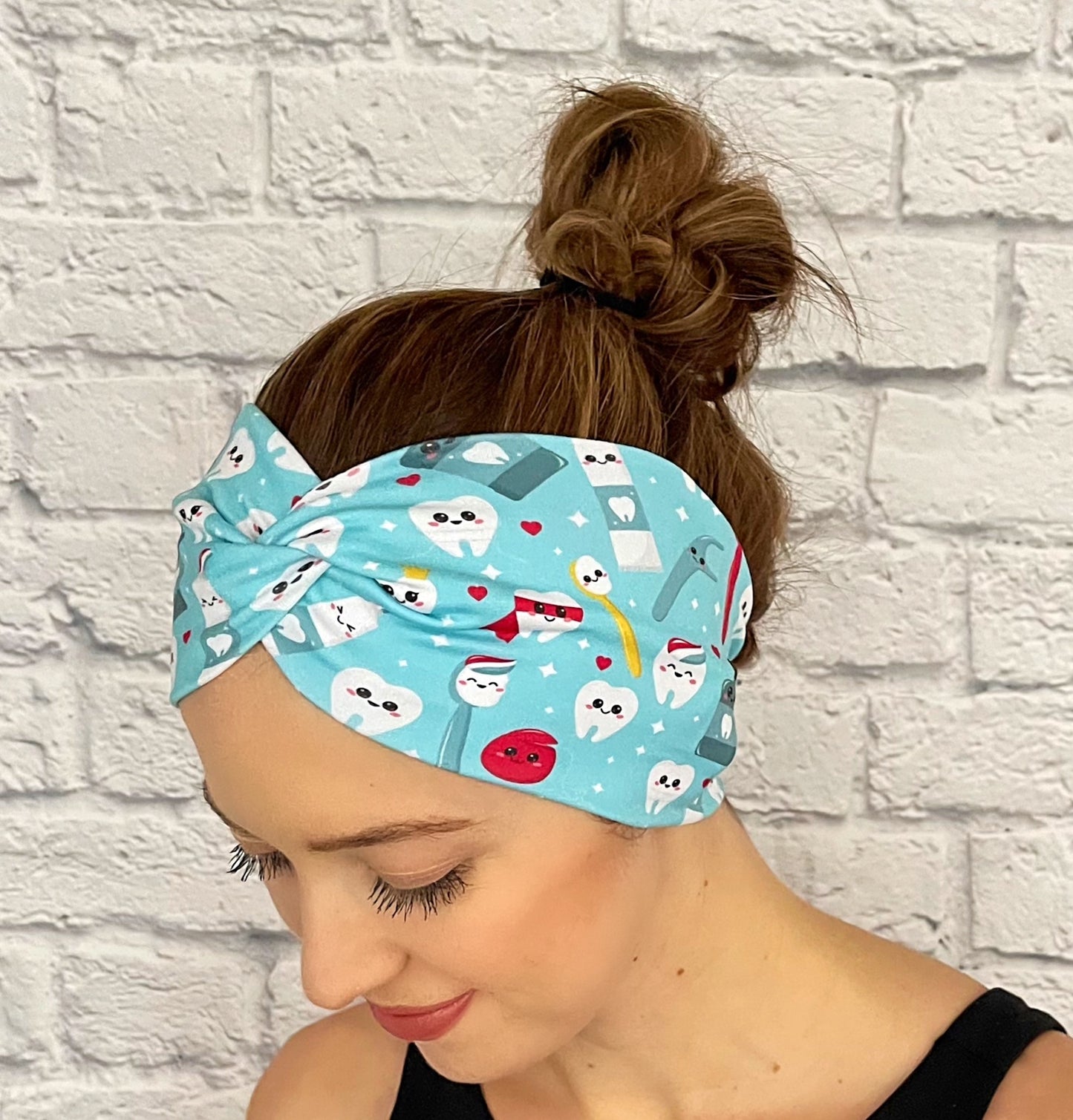 Woman with hair in bun wearing wide, twisted headband in light blue with dental theme print.