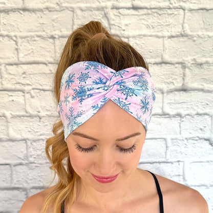 Woman wearing wide, twisted headband with blue, purple, and pink color with blue and white snowflake print.
