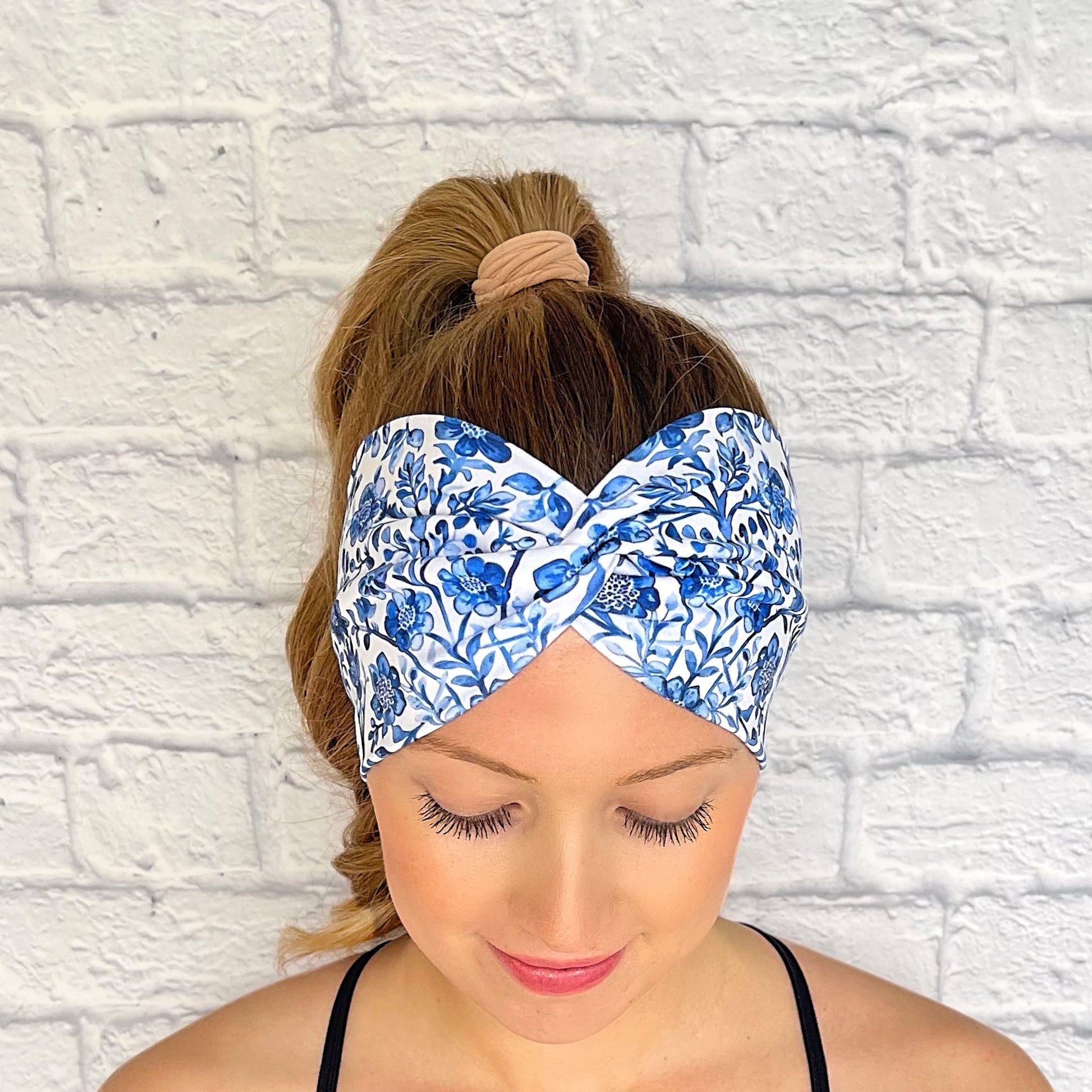 Woman with hair in curled ponytail wearing white, wide, twisted headband with blue floral print.