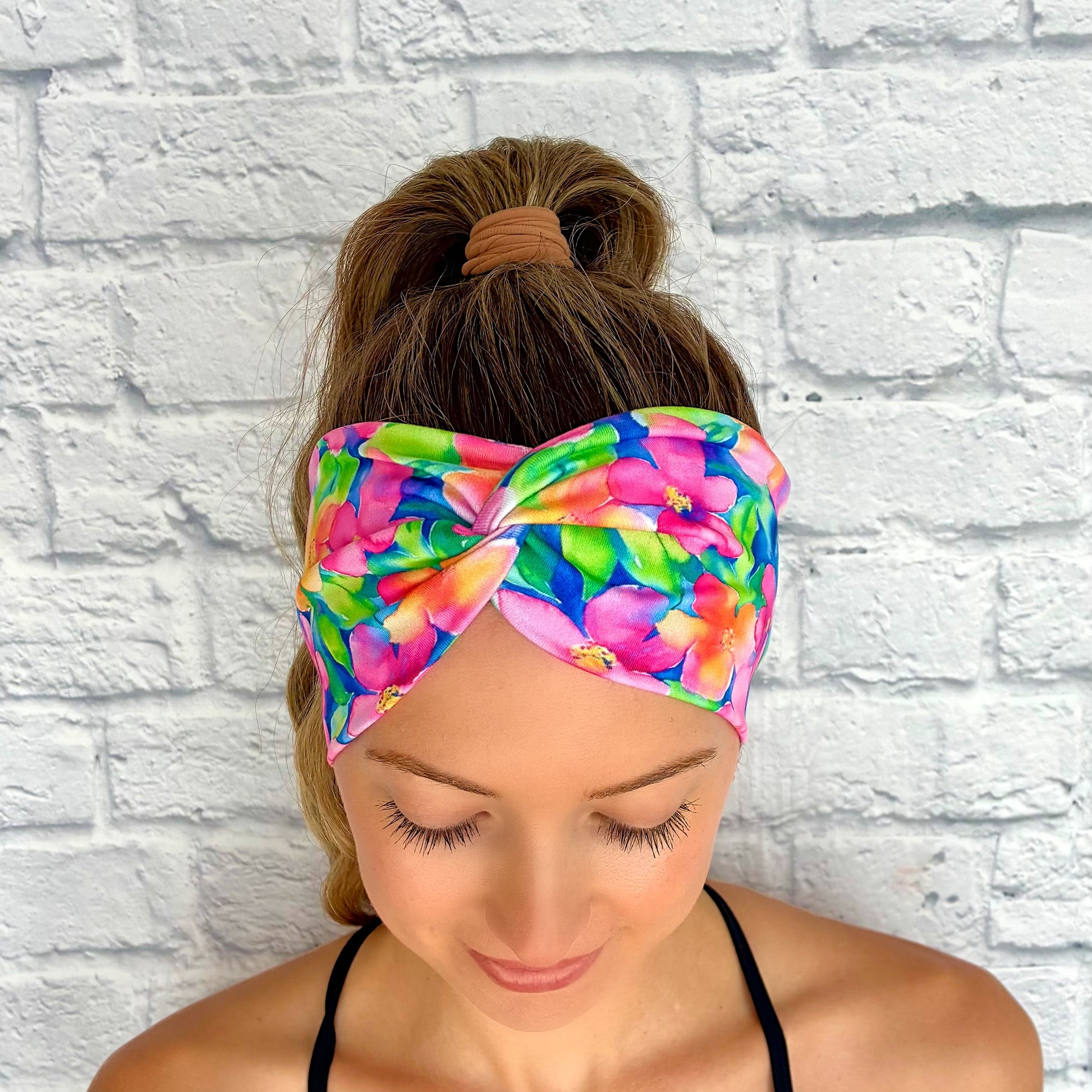 Woman with hair in ponytail wearing wide, twisted headband in blue with bright, multi-color Hawaiian theme floral print.