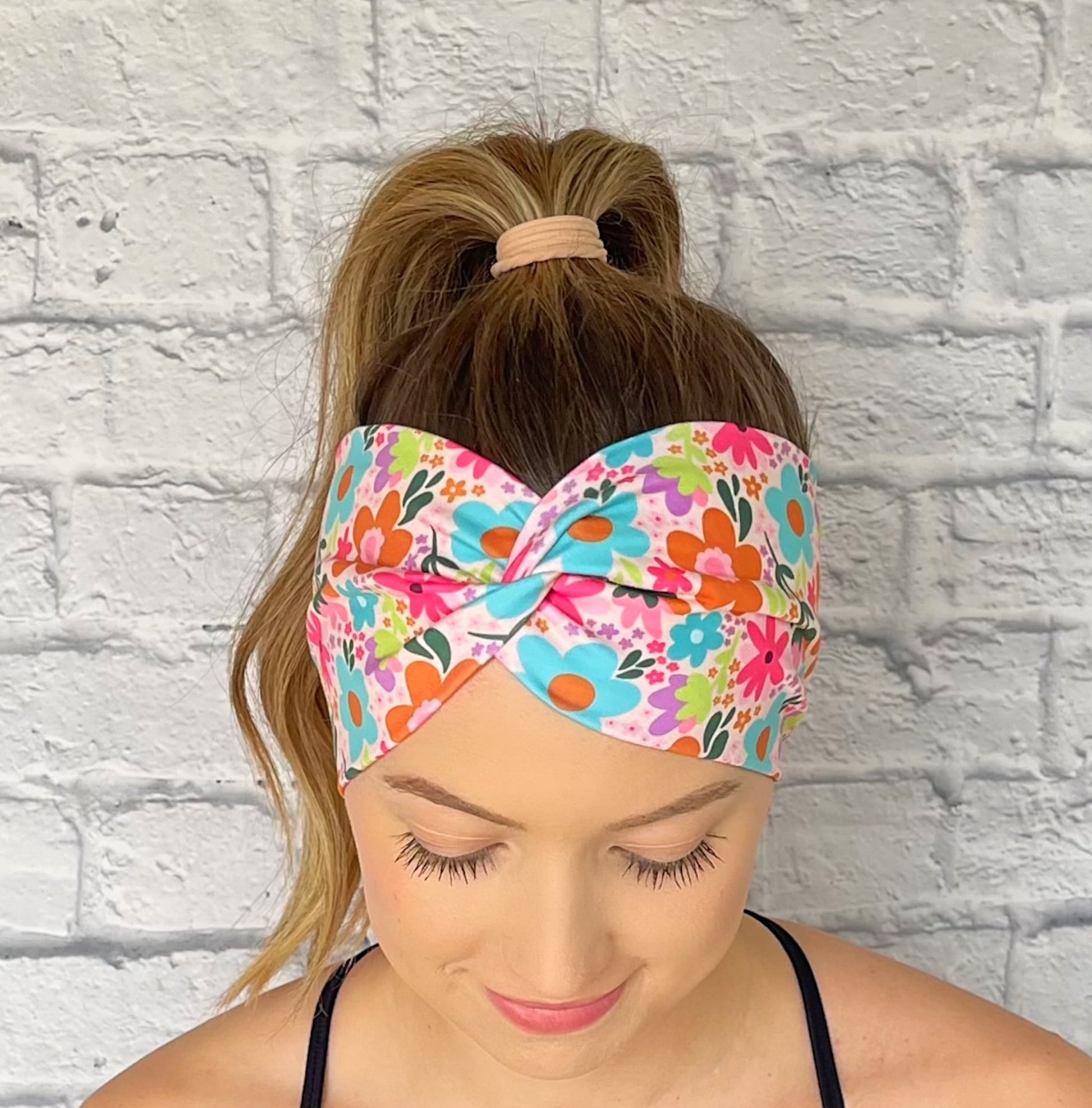 Woman wearing a colorful floral headband against a white brick wall.