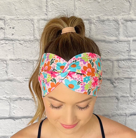 Woman wearing a colorful floral headband against a white brick wall.