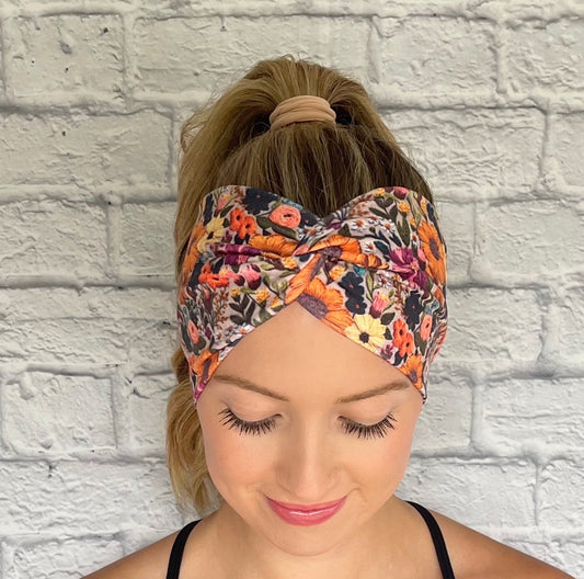 Woman with hair in ponytail wearing wide, twisted headband with faux embroidered, floral print.
